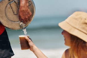 Una mujer vertiendo una bebida en una taza en la playa