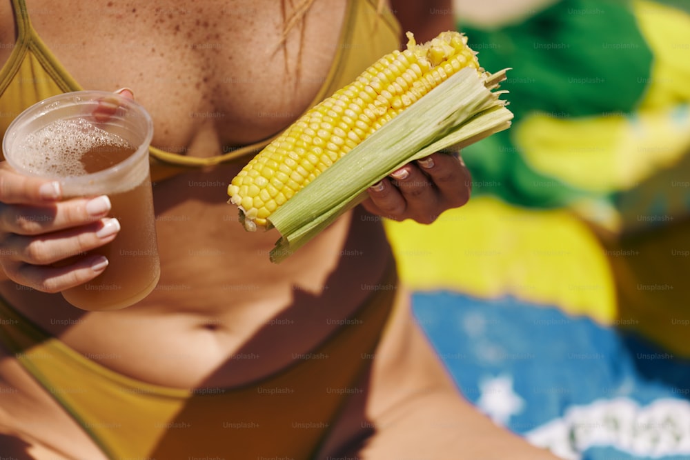 a woman holding a glass of beer and a corn on the cob