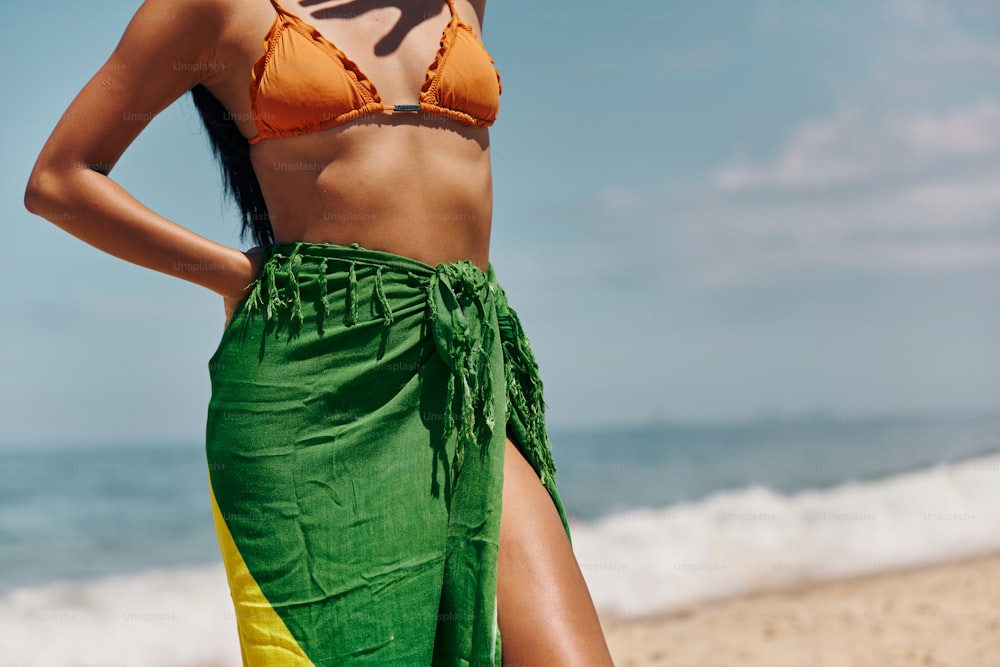 a woman in a bikini top and green skirt standing on the beach