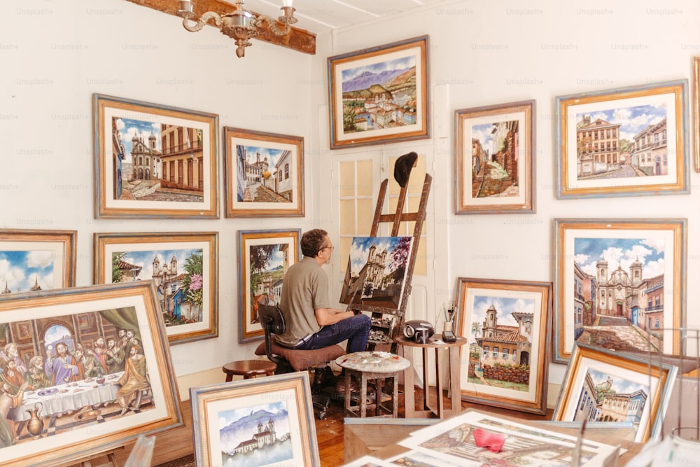 a man sitting in a chair in front of a wall of paintings