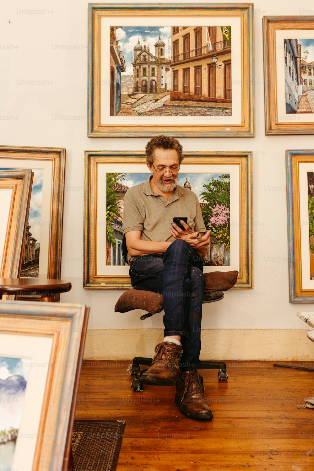 um homem sentado em uma cadeira na frente de uma parede de pinturas