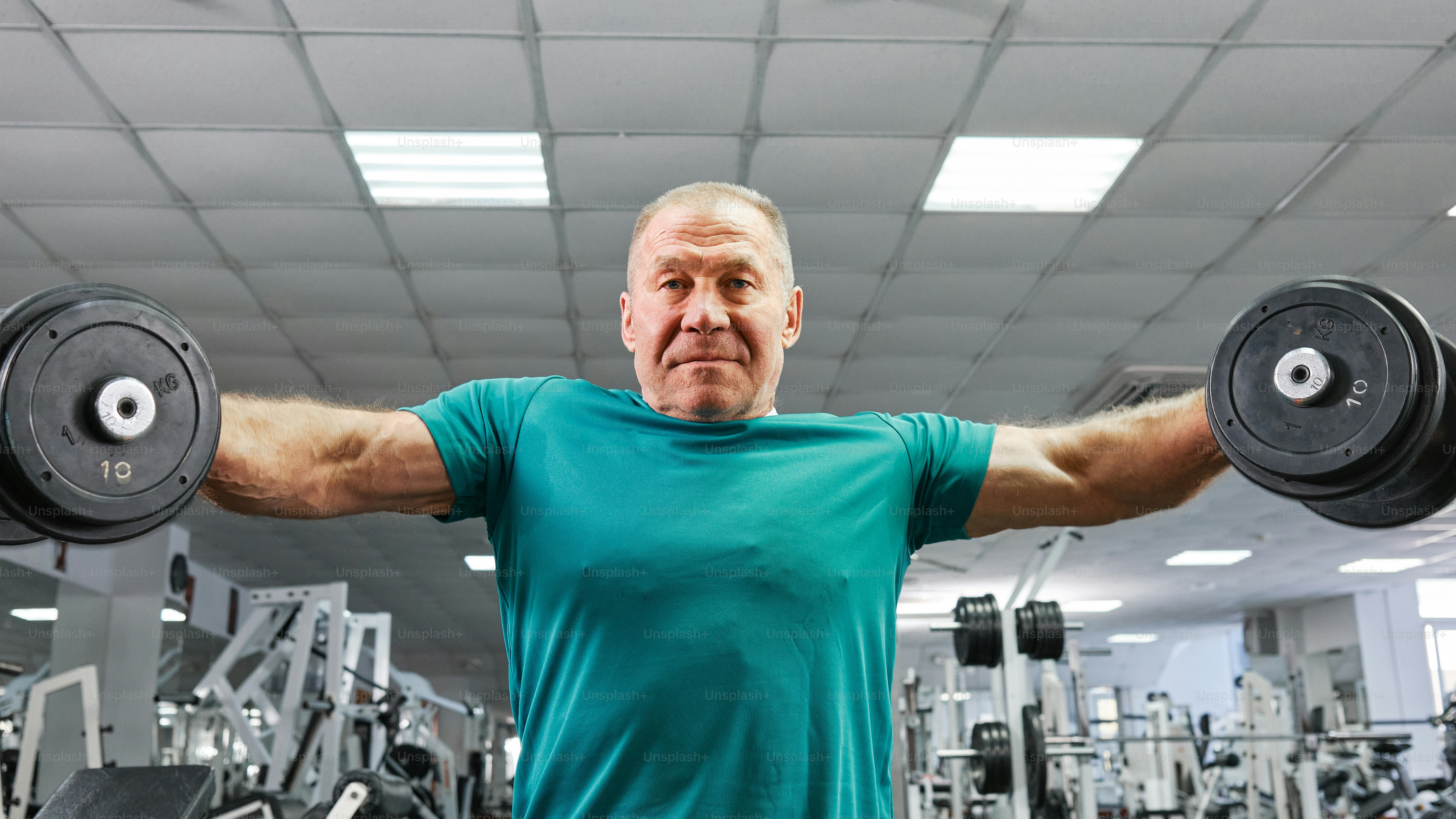 A retired man doing exercises with dumbbells at the gym