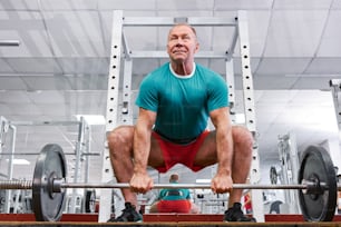 Un hombre se pone en cuclillas en una barra en un gimnasio