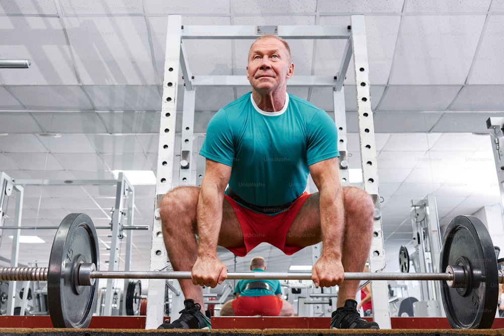 a man squats on a barbell in a gym