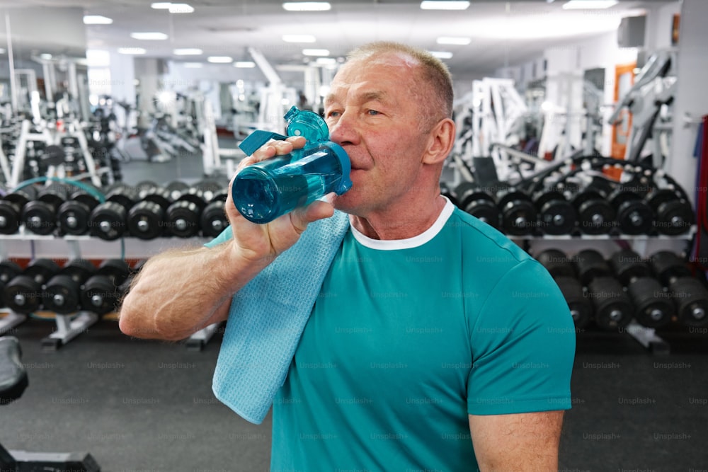 Ein Mann in einem Fitnessstudio, der aus einer Wasserflasche trinkt