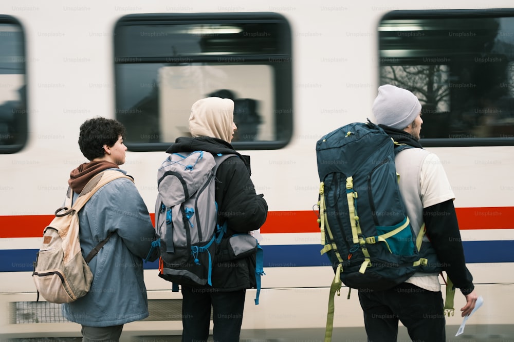 three people with backpacks waiting for a train