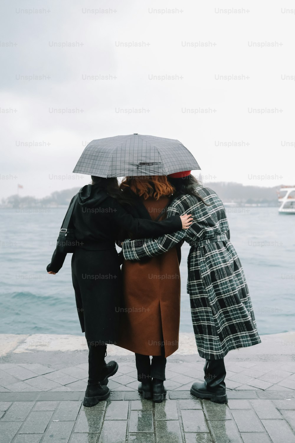 Tres personas de pie bajo un paraguas cerca del agua