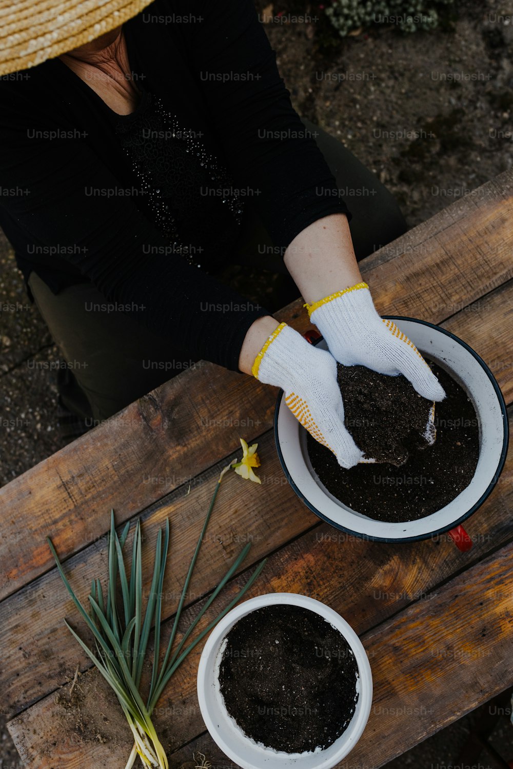 a person in a straw hat and white gloves scooping dirt into a white bowl