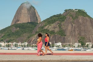 Un couple de femmes marchant sur une plage à côté d’une montagne
