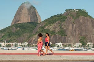 a couple of women walking down a beach next to a mountain