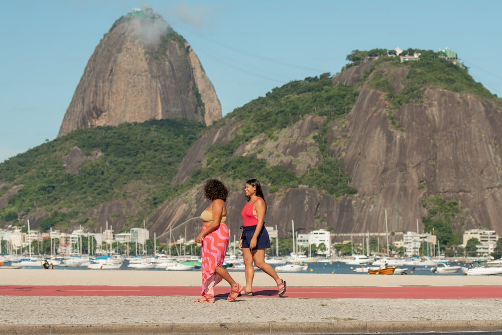 a couple of women walking down a beach next to a mountain