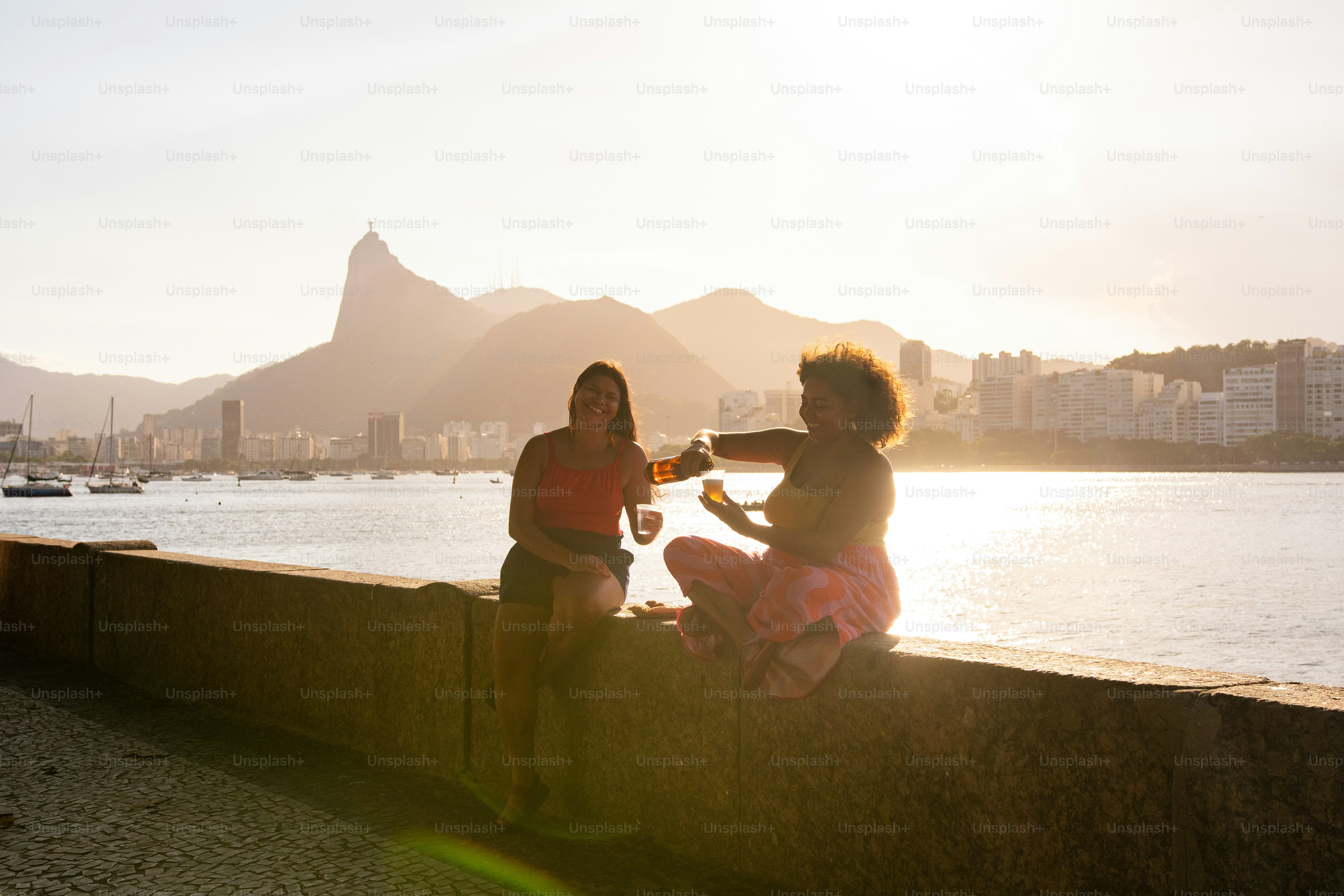 a couple of women sitting next to each other near a body of water