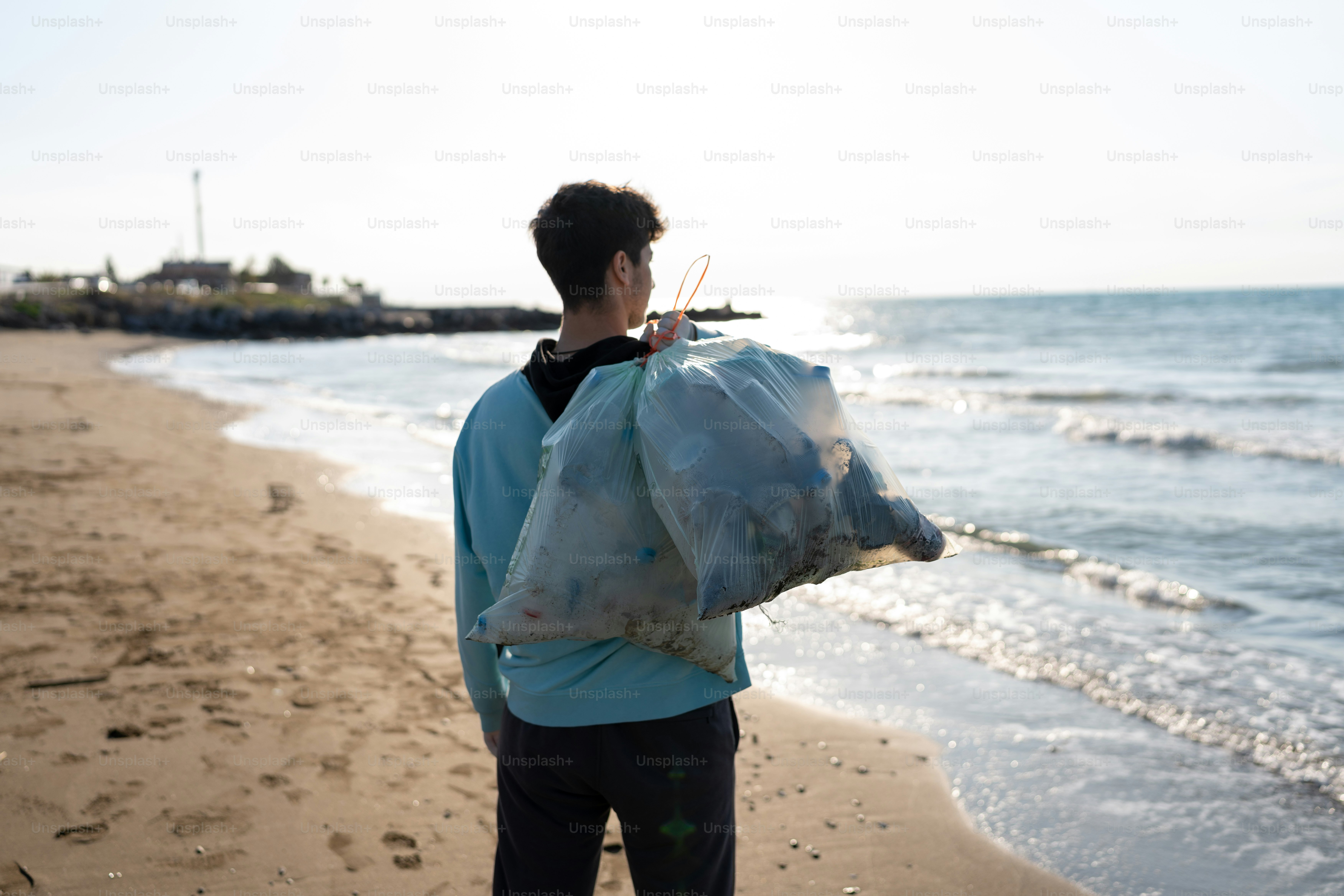 a man standing on a beach holding a bag of garbage