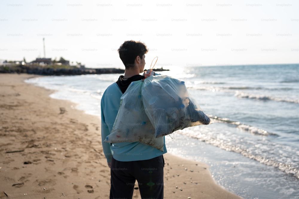 um homem de pé em uma praia segurando um saco de lixo