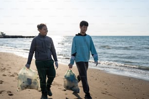 two people walking on a beach with bags of garbage