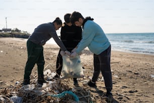 three people picking up trash on a beach