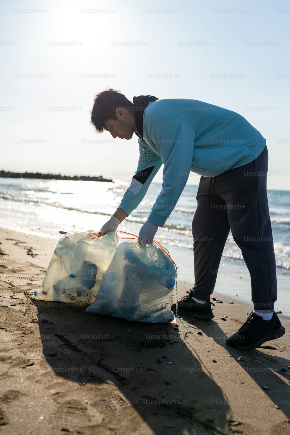 a man standing on a beach next to a bag of trash