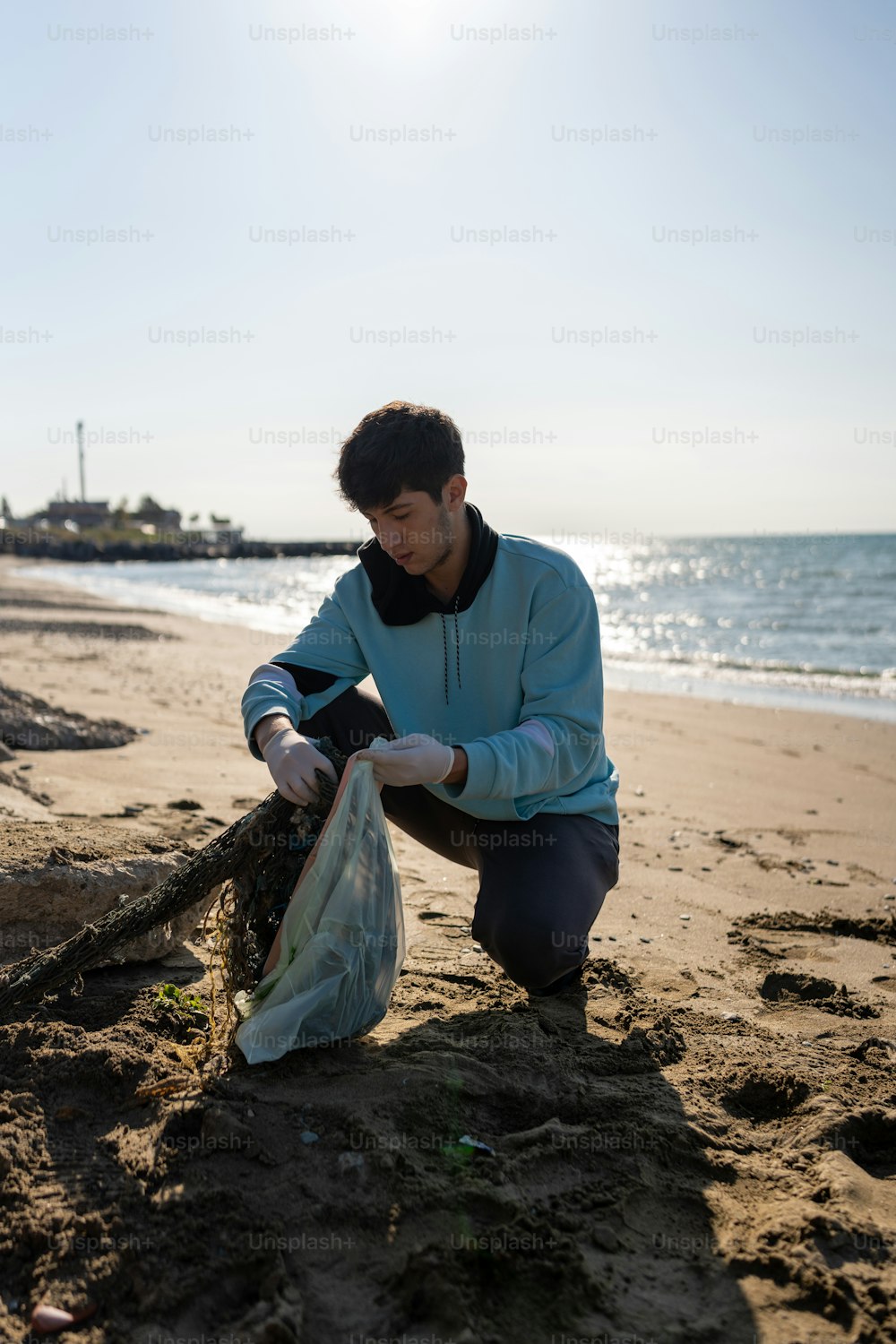 Un hombre arrodillado en una playa junto a una bolsa