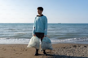 a man standing on a beach holding two bags of garbage