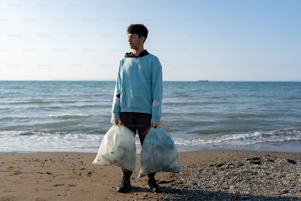 a man standing on a beach holding two bags of garbage