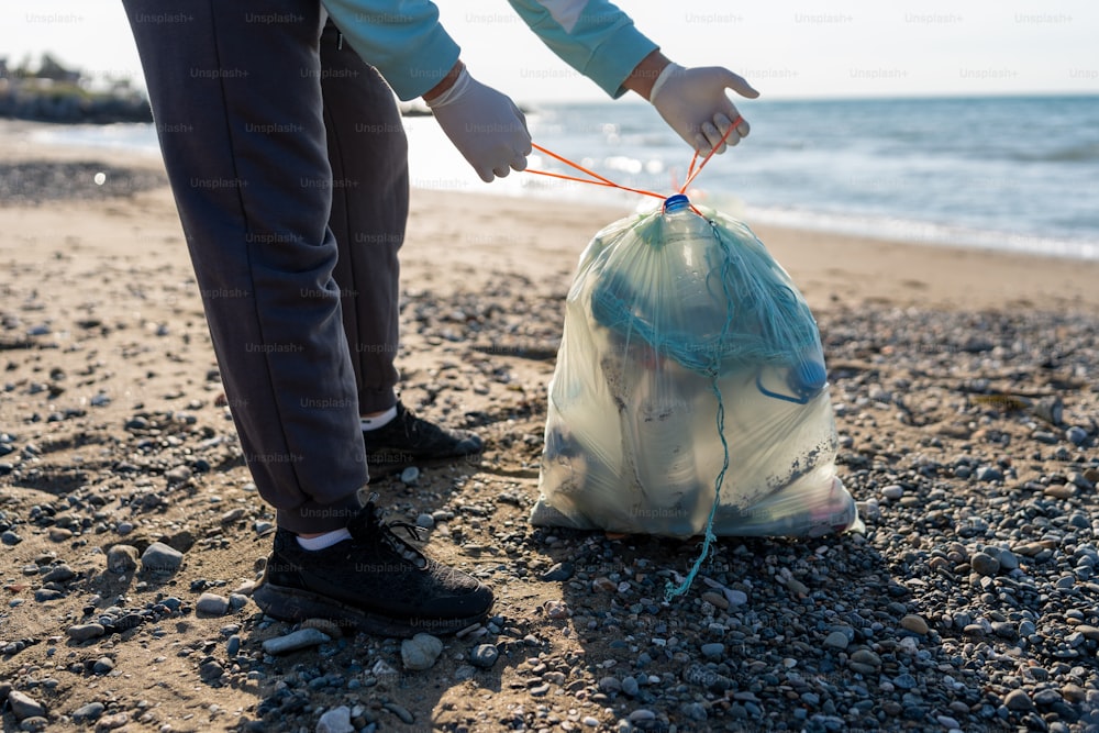 eine Person, die mit einem Sack Müll am Strand steht