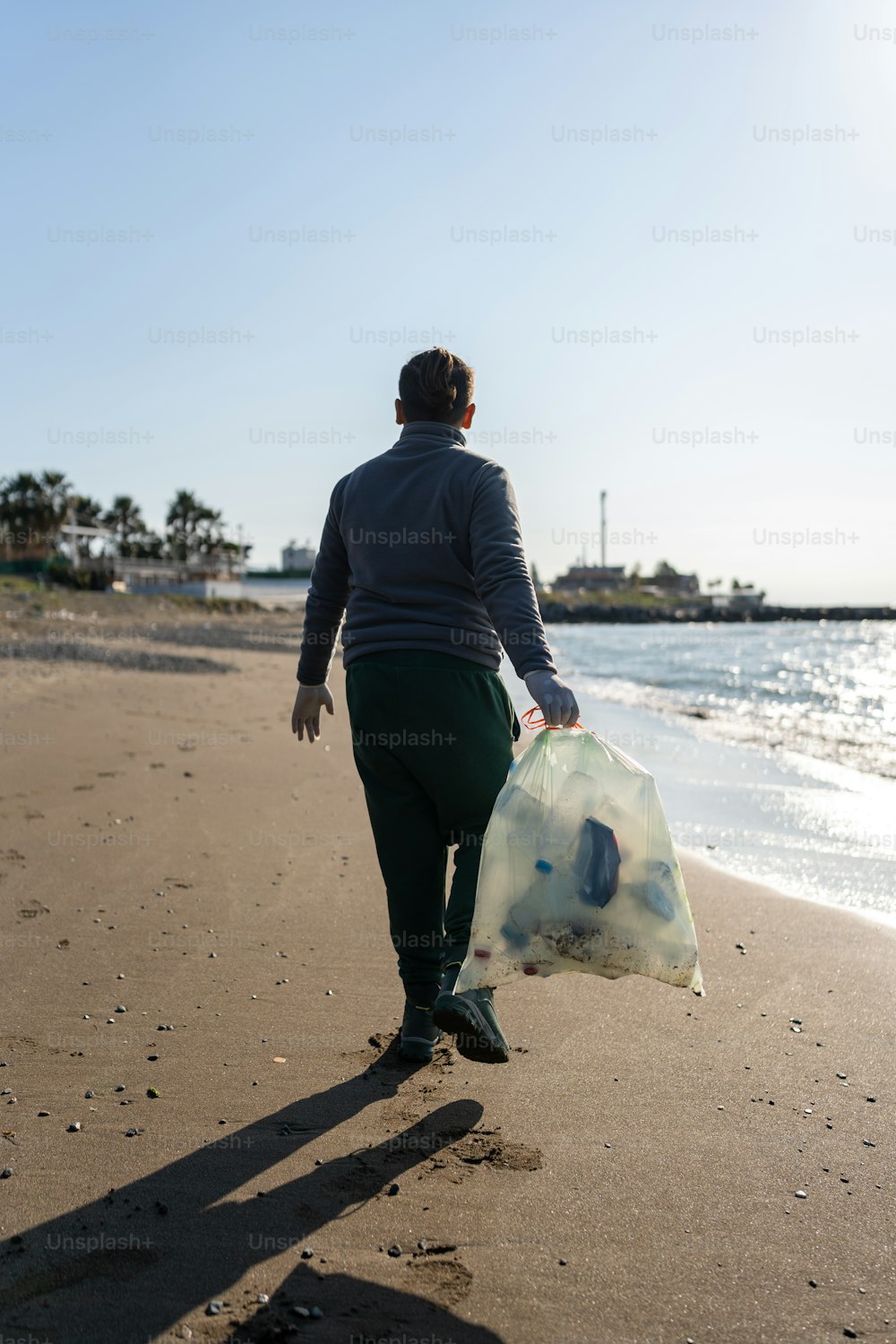 um homem andando em uma praia carregando um saco de lixo