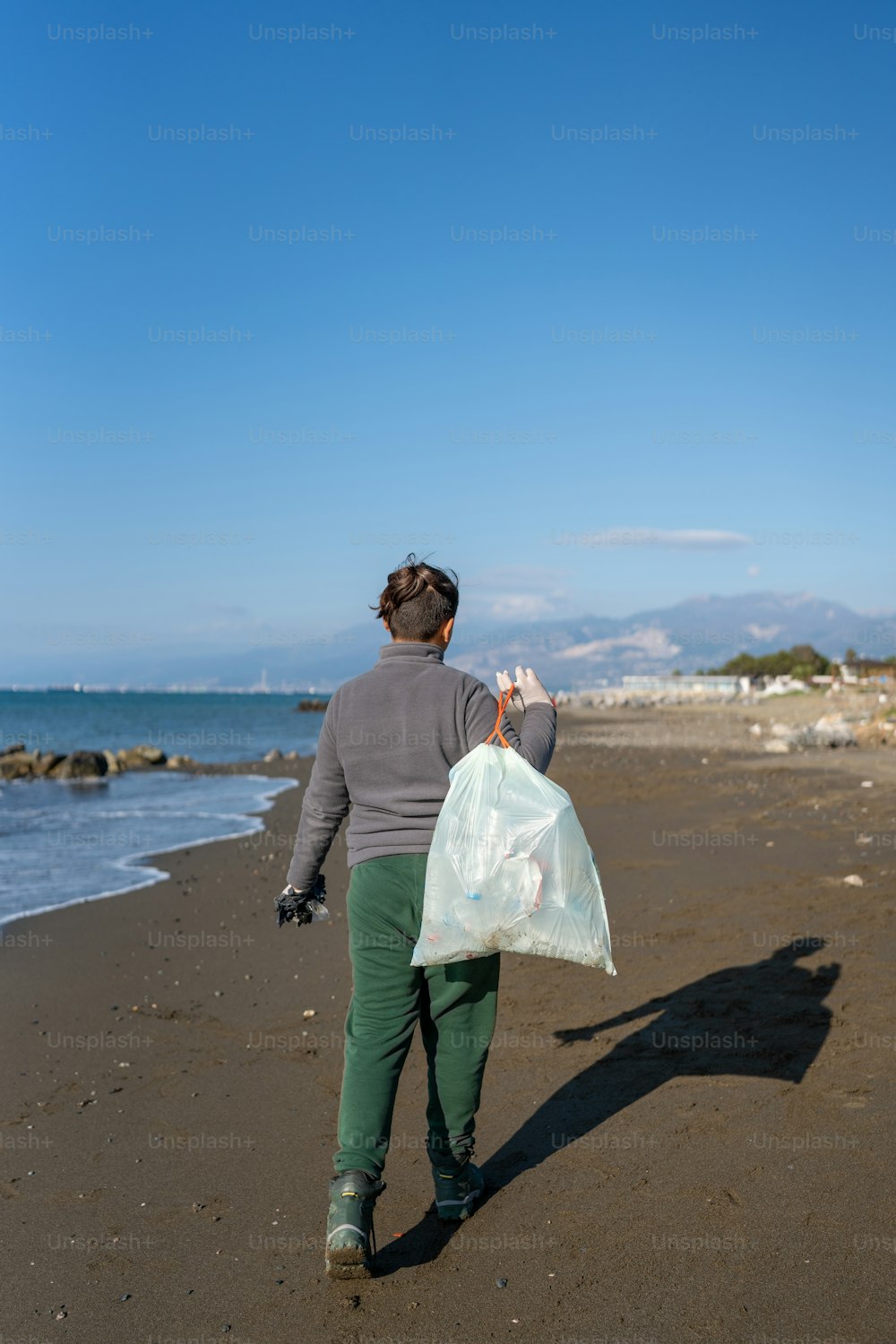 una persona che cammina su una spiaggia con un sacchetto di plastica