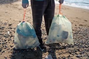 eine Person, die zwei Säcke Müll an einem Strand hält