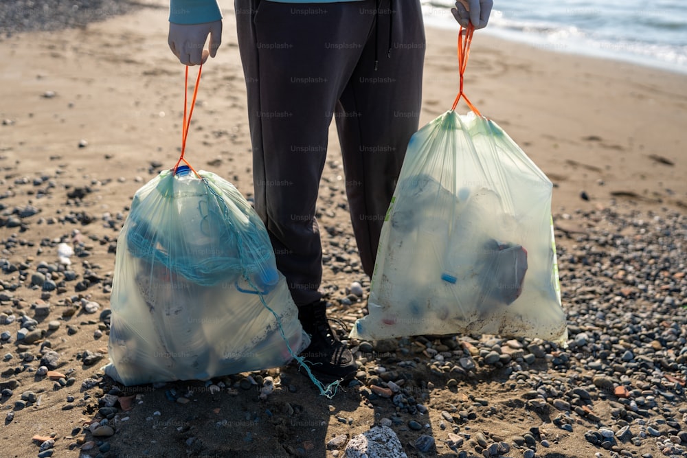 una persona che tiene due sacchi di immondizia su una spiaggia