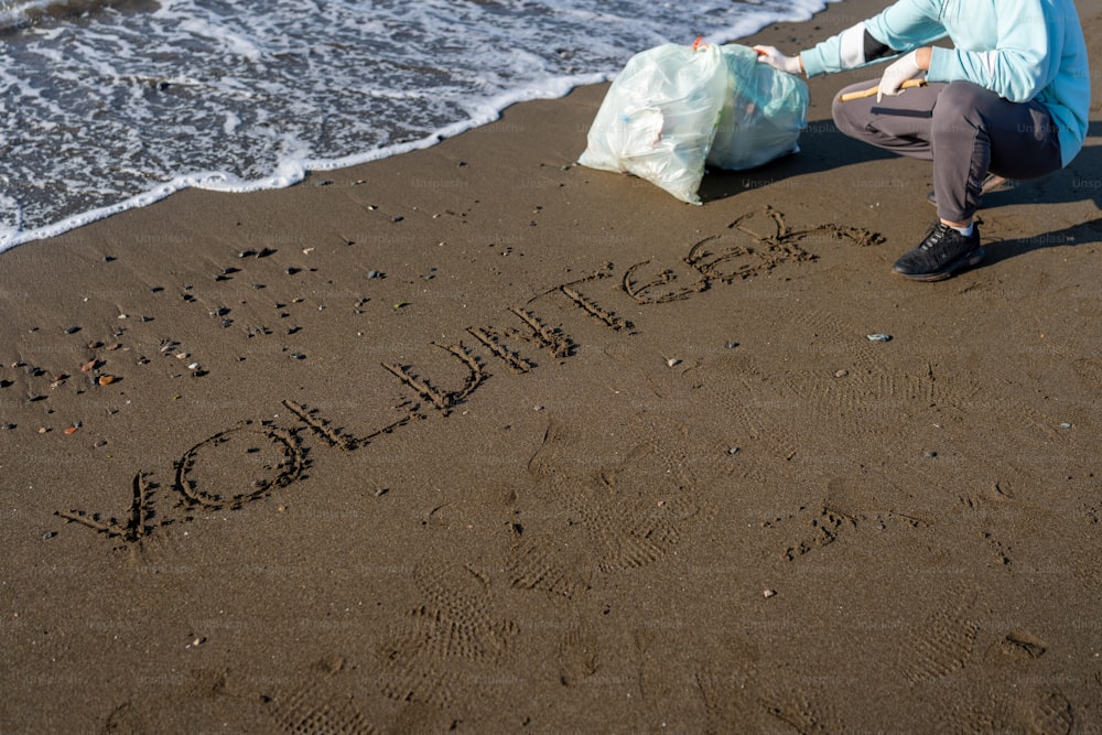 Una mujer arrodillada en una playa escribiendo en la arena