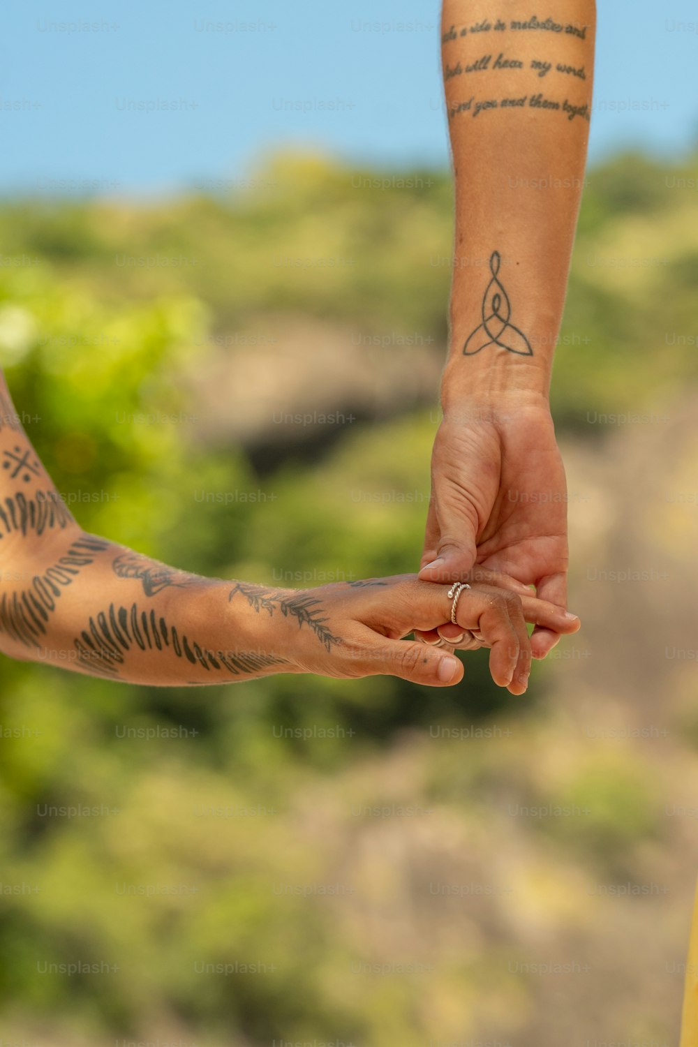 two people holding hands with tattoos on their arms
