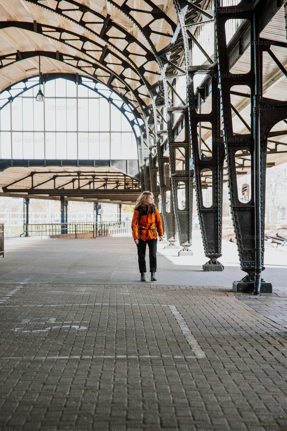 주황색 재킷을 입은 남자가 기차역을 걷��고 있다