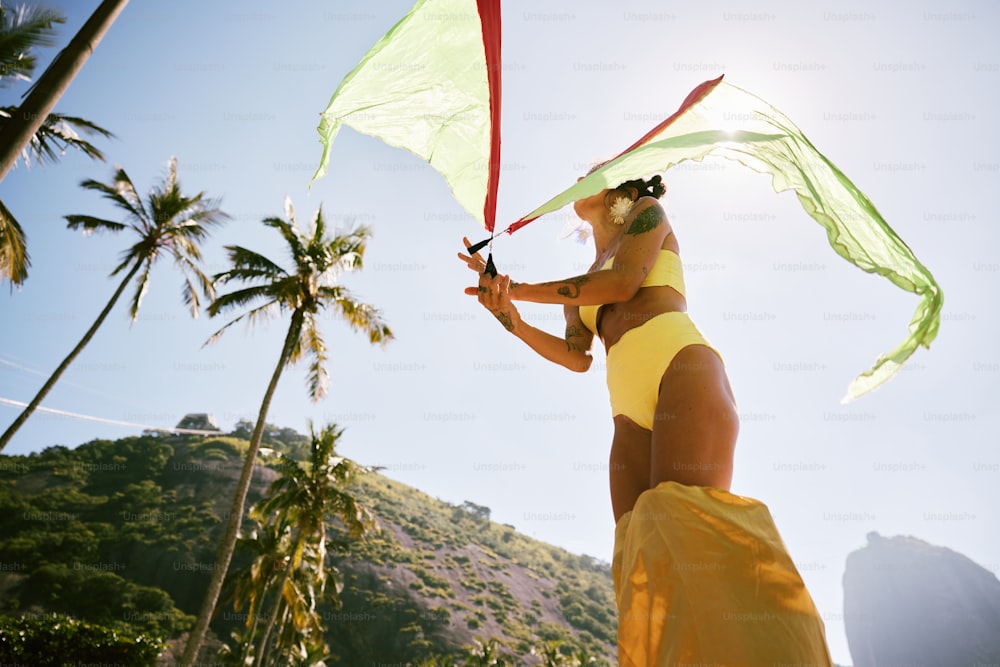 uma mulher em um biquíni amarelo segurando uma pipa verde e vermelha