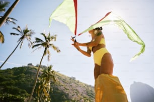 a woman in a yellow bikini holding a green and red kite