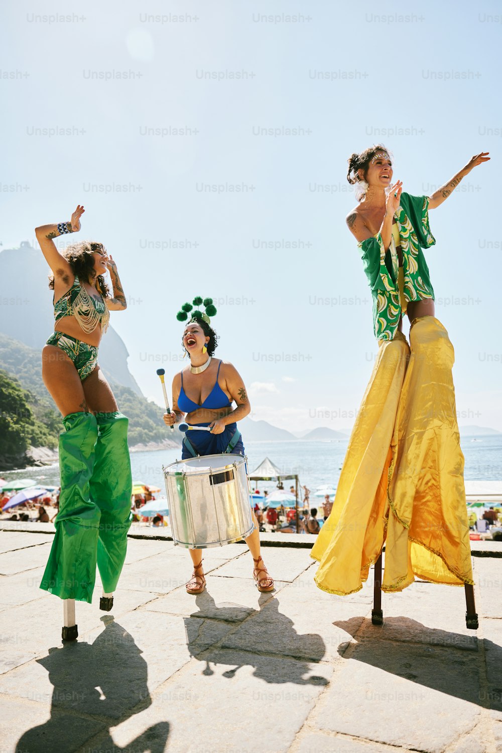 緑と黄色の衣装を着た3人の��女性がドラムを演奏