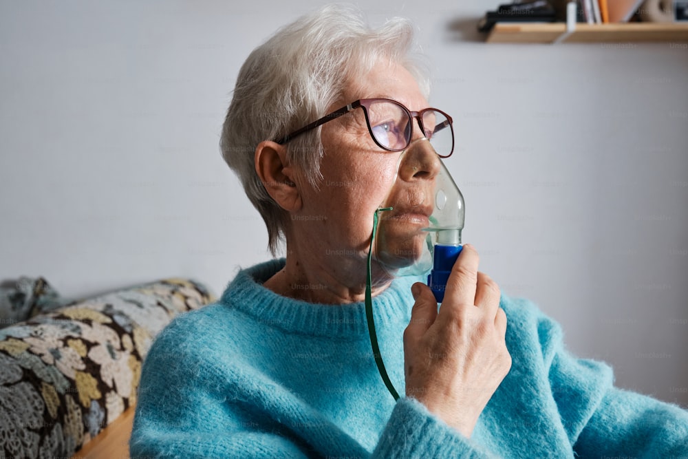 uma mulher idosa que usa óculos segurando um objeto azul em sua mão