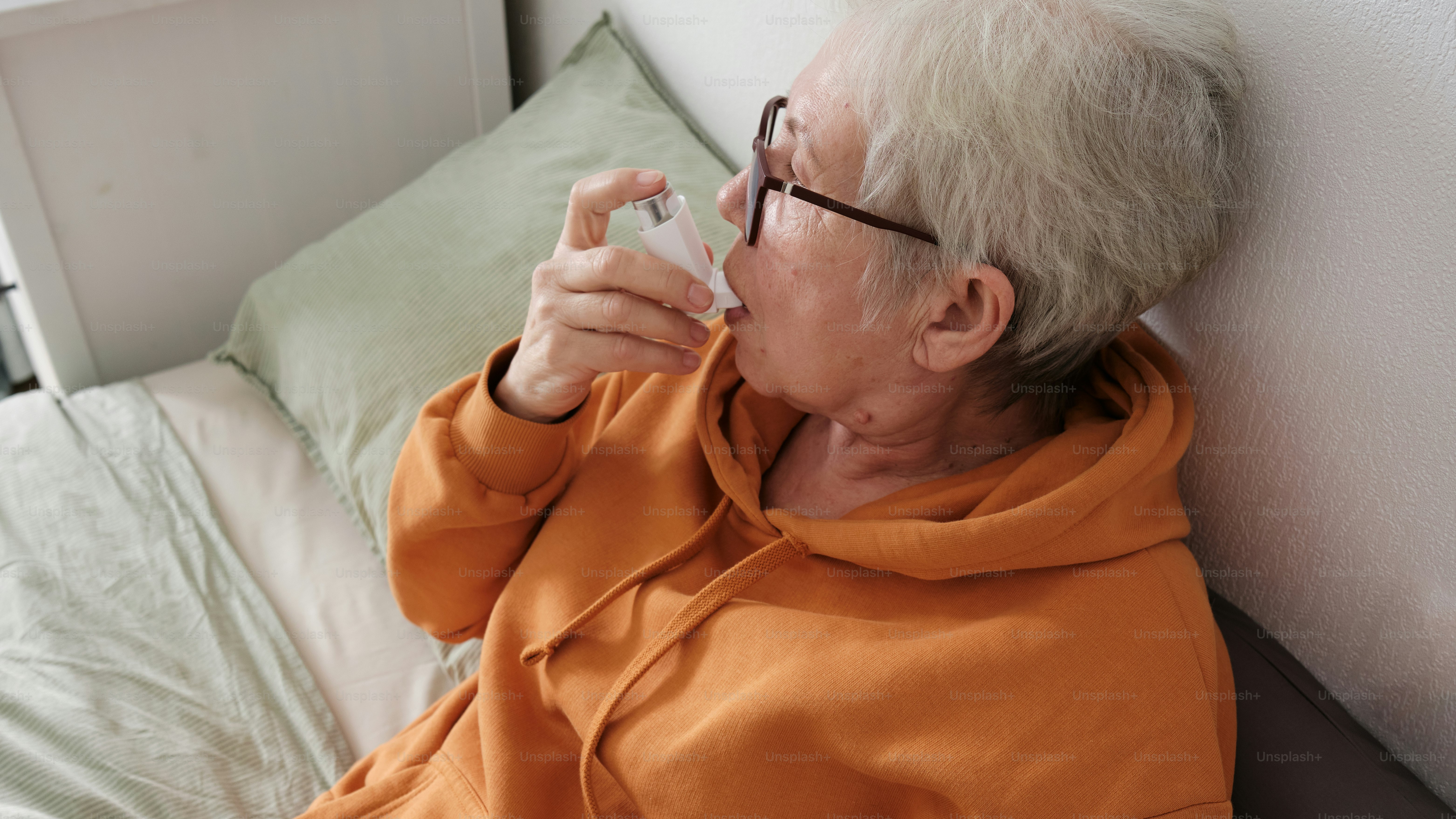 a woman in an orange shirt is sitting on a bed using an inhaler
