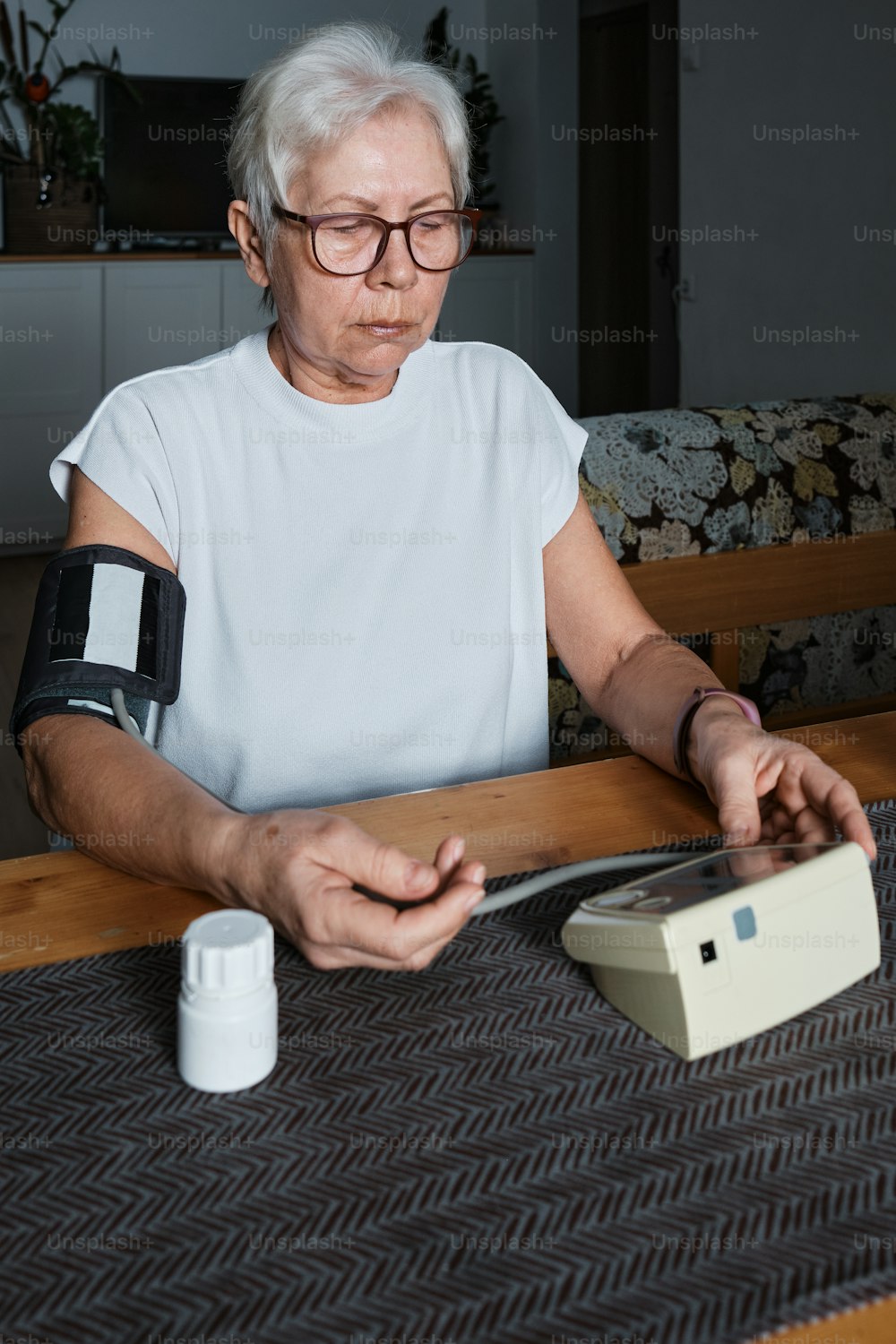 an elderly woman sitting at a table with an electronic device
