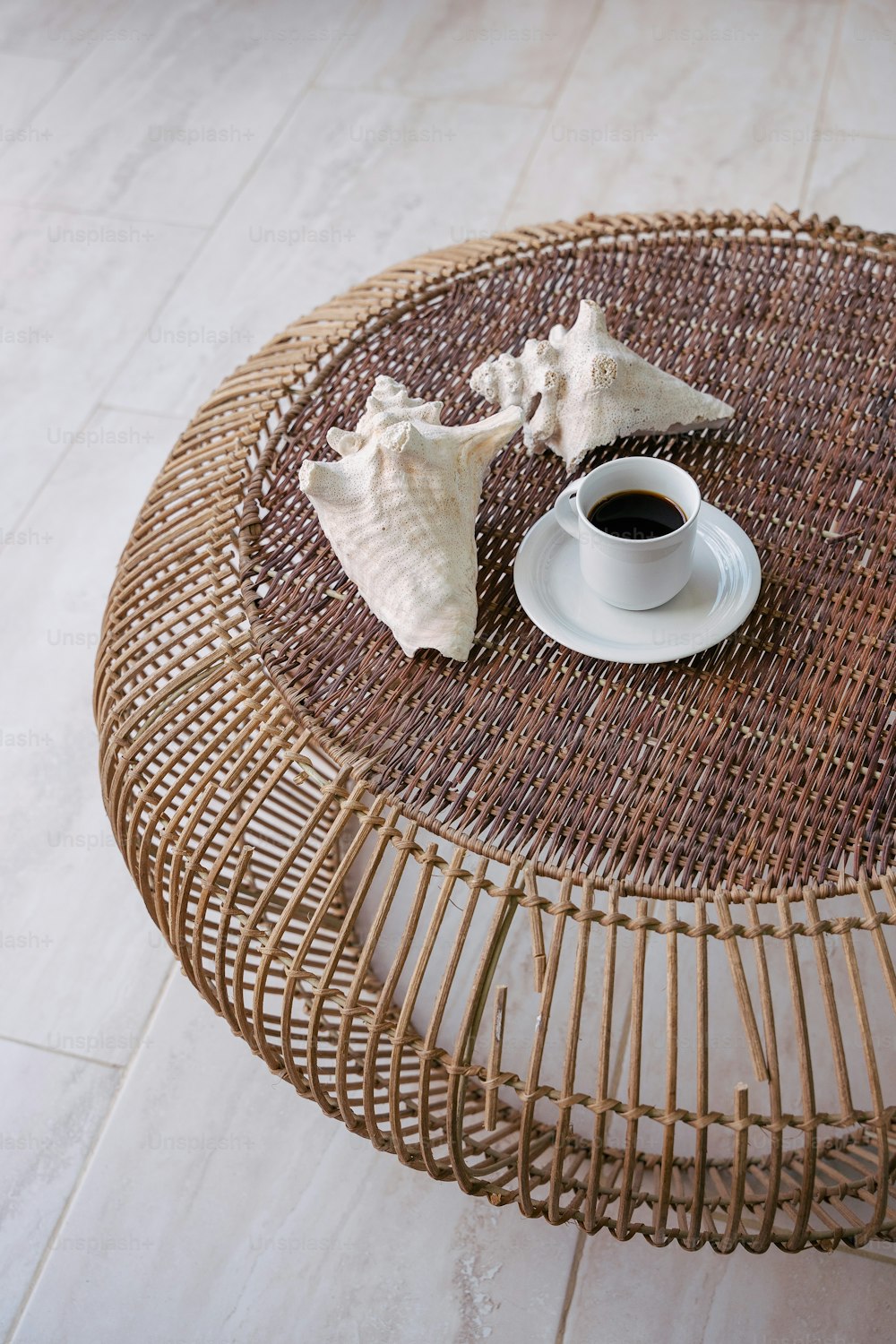 a wicker table with a cup of coffee and seashells on it