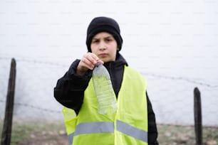 a boy in a yellow vest holding a plastic bottle