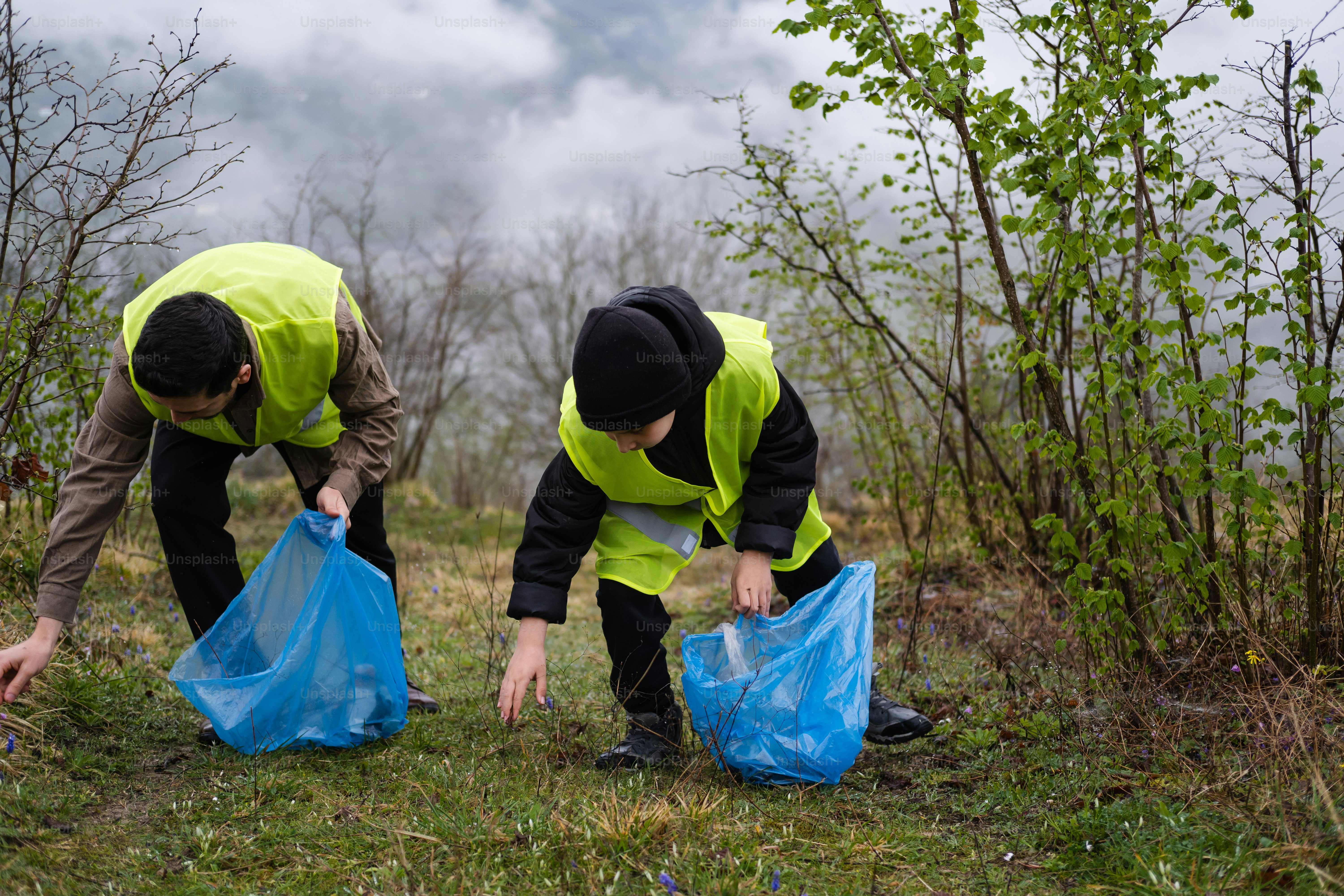 Zwei Männer in gelben Westen heben Plastiktüten auf