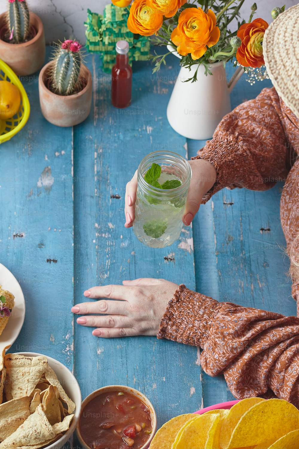 Una donna tiene in mano una tazza di bevanda mentre è seduta a un tavolo pieno di cibo