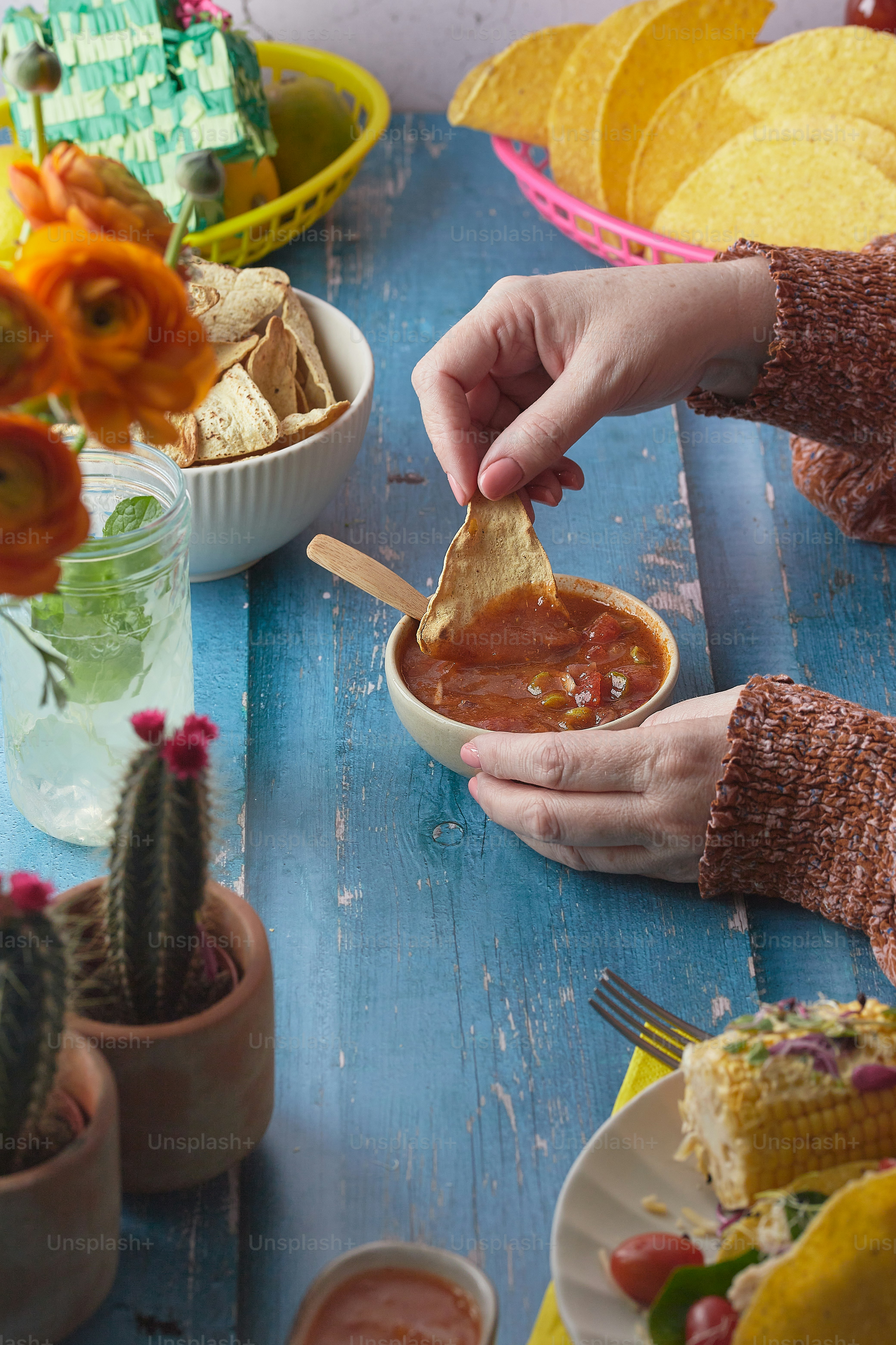 Eine Person, die eine Tortilla in eine Schüssel Salsa taucht