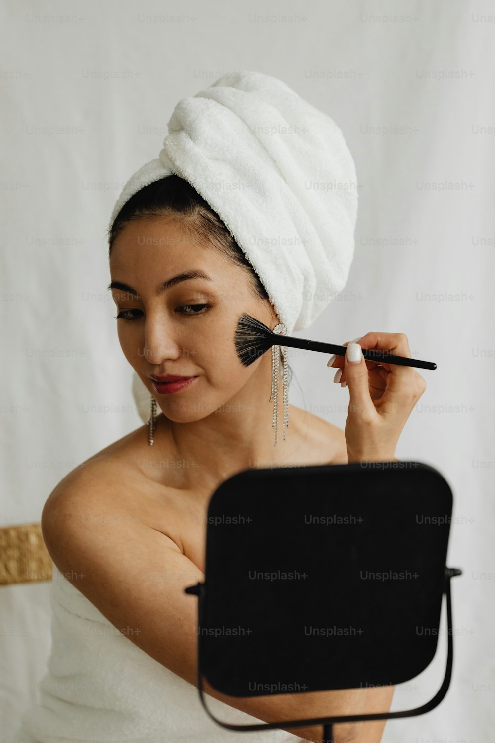 a woman with a towel on her head brushes her face with a brush