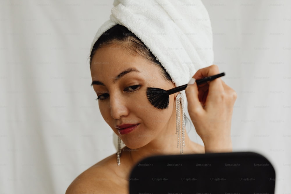 uma mulher com uma toalha na cabeça escova o rosto com um pincel