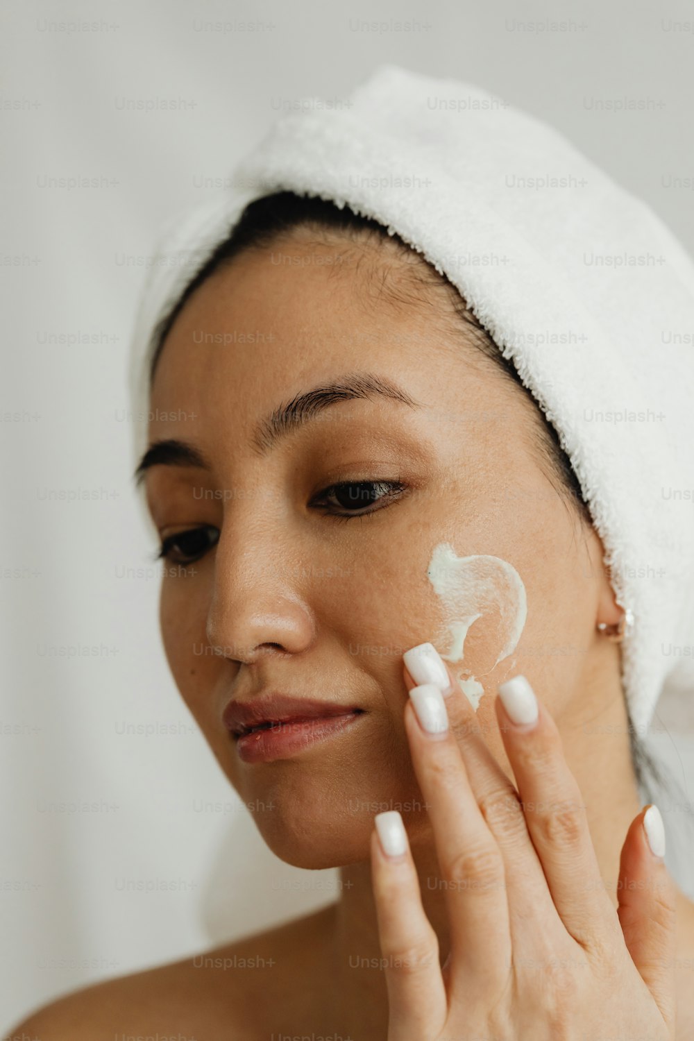 une femme avec une serviette sur la tête appliquant une crème sur son visage