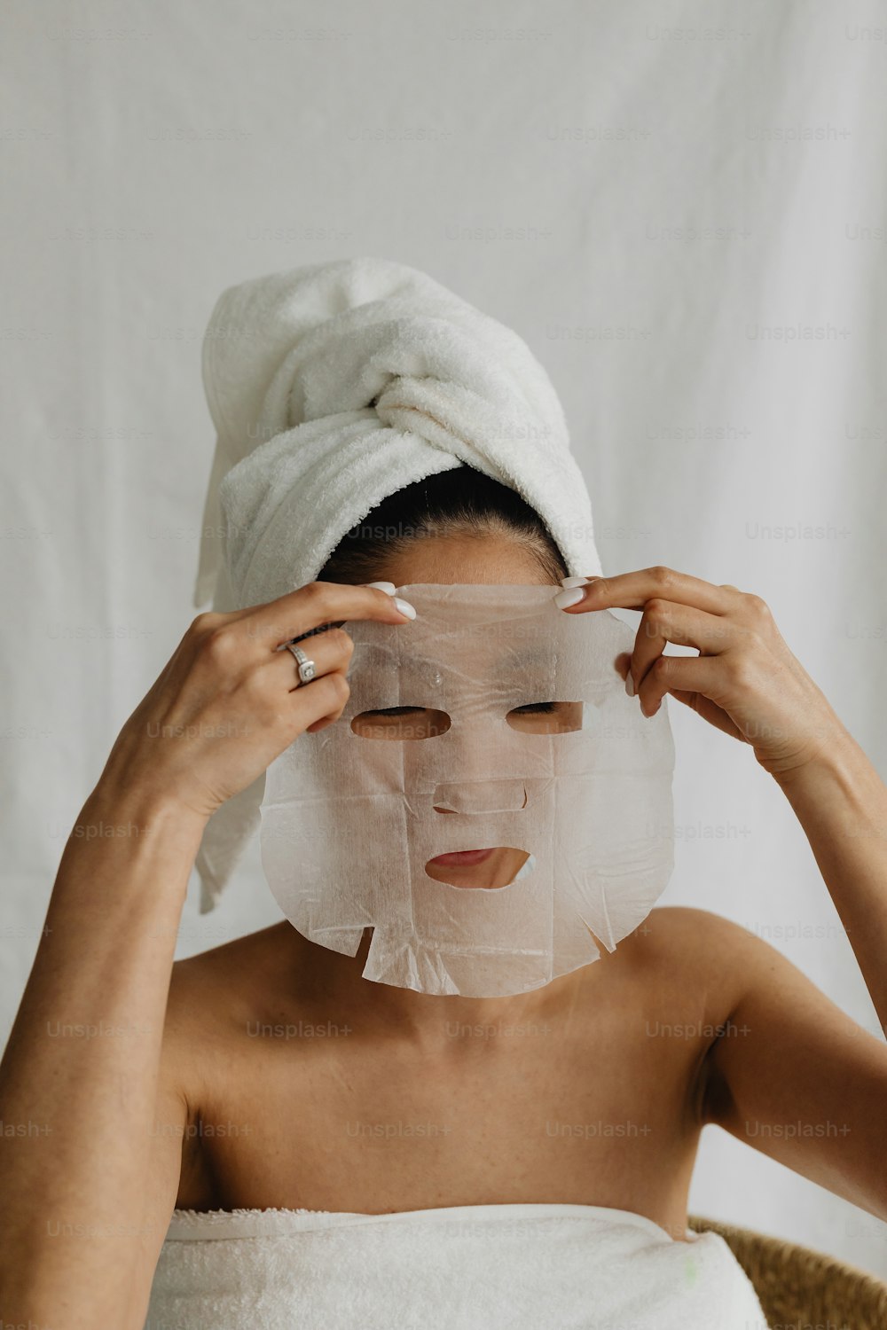 Una donna con un asciugamano in testa si copre il viso con un lenzuolo di