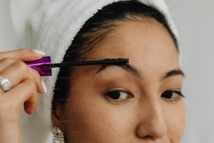 a woman with a towel on her head is putting mascara on her forehead