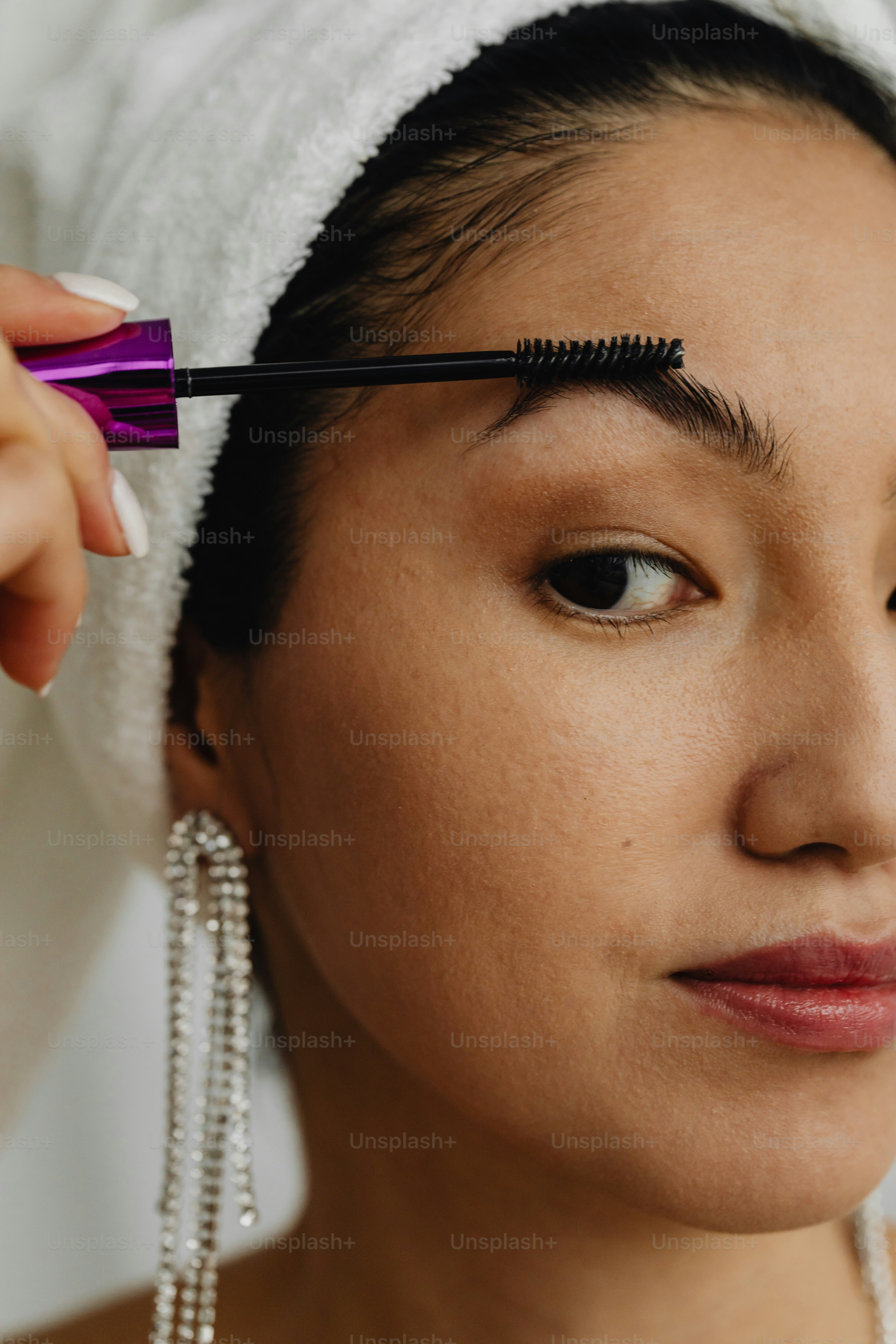 a woman with a towel on her head and a mascara in her hand