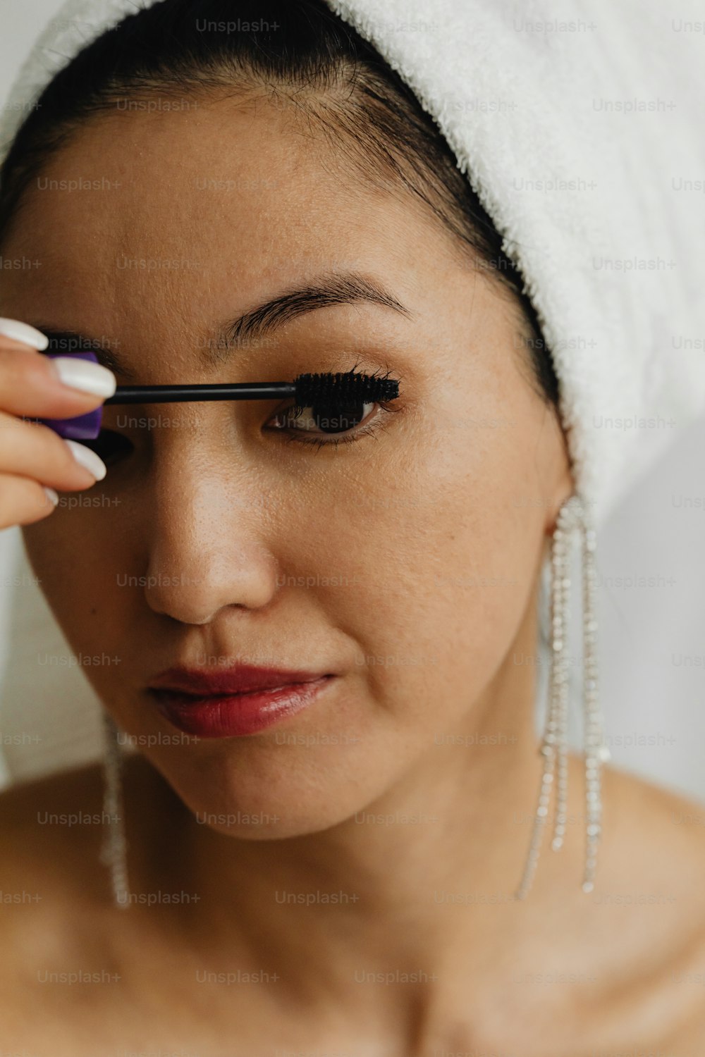 Une femme avec une serviette sur la tête mettant du mascara sur son œil